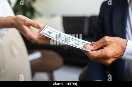 Caucasien vieil homme d'affaires en costume donne de l'argent dollars en espèces à la main de femme dans l'intérieur de bureau, close up Banque D'Images