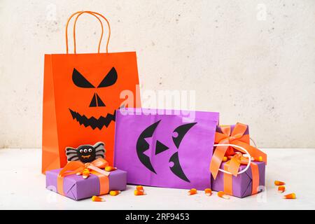 Composition avec des sacs à provisions, des boîtes-cadeaux et des cors de bonbons savoureux pour Halloween sur fond clair Banque D'Images