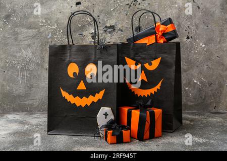 Composition avec sacs à provisions, boîtes cadeaux et cookie savoureux pour Halloween sur fond gris grunge Banque D'Images