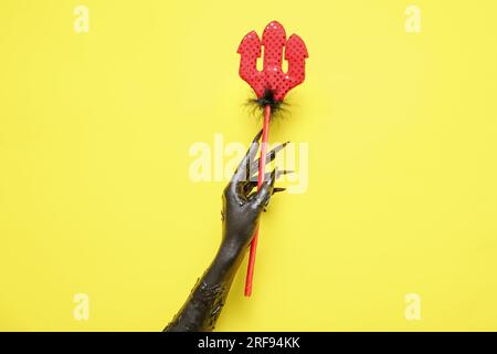 Main noire de sorcière avec la fourche du diable sur fond jaune. Fête d'Halloween Banque D'Images