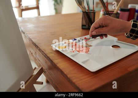Main de femme créative mélangeant des peintures avec un couteau à palette Banque D'Images