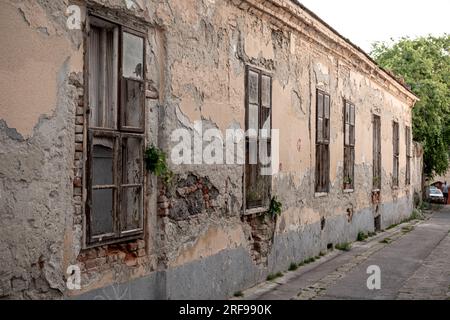 Extérieur du bâtiment abandonné vieilli avec des murs en pierre en ruine et de petites fenêtres situé sur la rue de la petite ville Banque D'Images