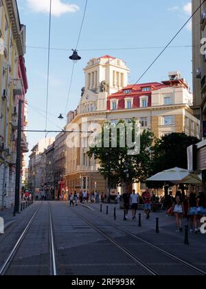 Rue pleine de piétons dans le centre de la ville de Sofia avec un élégant bâtiment de banque coloré, et des pistes de tramway Bulgarie. 1 août 2023. Banque D'Images