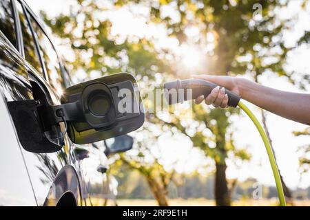 Jeune femme brancher le chargeur dans une voiture électrique noire, concept d'énergie renouvelable Banque D'Images