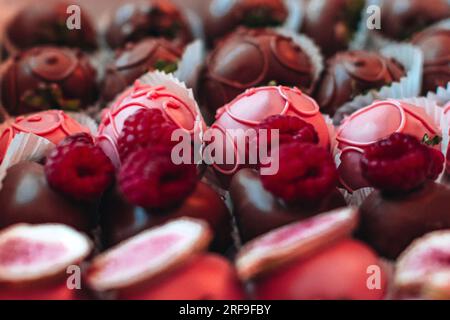 Fraises recouvertes de chocolat rose avec des framboises fraîches sur le dessus. Collection de bonbons et de bonbons. Ensemble savoureux pour les vacances. Macro Banque D'Images