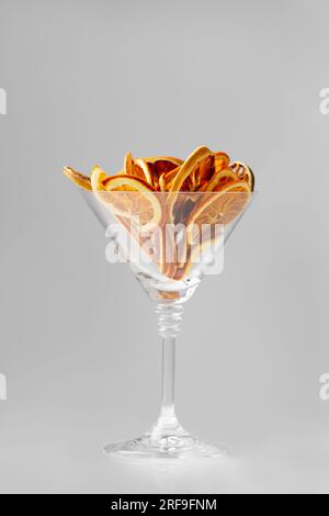 Copeaux d'orange secs isolés. Copeaux d'orange dans un verre à martini sur fond blanc. Une nutrition adéquate. Chips de fruits. Tranches sèches aux agrumes. Banque D'Images