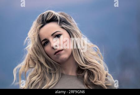 Graceful Beauty : Serene Young Blonde Woman pose avec réflexion sur un fond bleu Banque D'Images