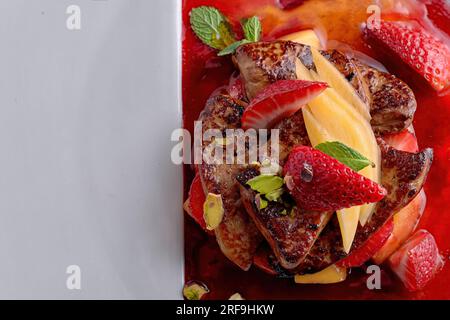 Foie gras de canard à la sauce fraise avec morceaux de poire et de fraise sur la plaque blanche Banque D'Images