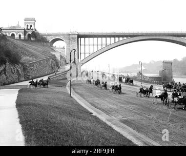 New York, New York : c. 1905 vue du Harlem River Speedway avec le Washington Bridge en arrière-plan. Il était initialement ouvert uniquement aux voitures et aux sulkies afin que les riches puissent faire défiler leurs chevaux de Trotting sur la route de terre de 2,5 km. Les piétons, les cavaliers et les cyclistes étaient interdits. Banque D'Images