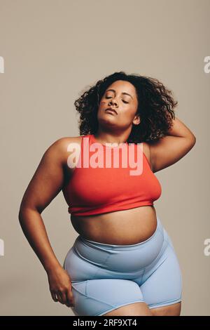 Vêtue de vêtements de sport, une femme confiante se tient en toute confiance dans un studio, embrassant son corps en forme. Jeune femme sportive s'acceptant elle-même comme elle embrasse Banque D'Images