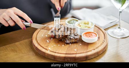 Déjeuner dans un restaurant, une femme mange des morceaux de foie cuits sur le grill. Servir sur une planche de bois. Restaurant Barbecue menu, une série de photos de Banque D'Images