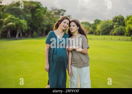 Un moment réconfortant capturé dans le parc comme une femme enceinte après 40 partage un lien spécial avec sa fille adolescente, embrassant la beauté de Banque D'Images