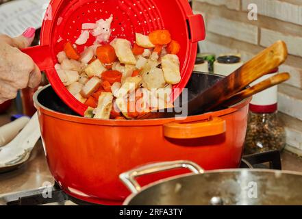 Le chef ajoute des légumes bouillis aux cuisses de poulet frites dans une poêle. Banque D'Images