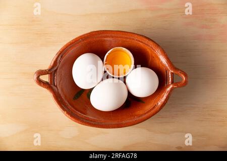 Quatre œufs de poule dans un récipient en argile sur une table en bois. Produit alimentaire nutritif et économique très populaire. vue de dessus de la table. Banque D'Images