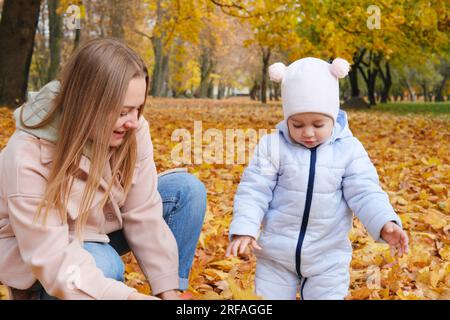 Une mère avec sa petite fille ramasse des feuilles dans le parc d'automne. Photo horizontale Banque D'Images