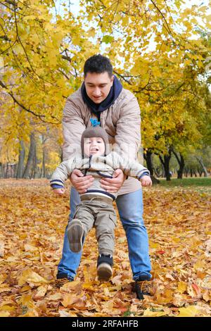 Père ramassant son fils tout en se tenant dans le parc d'automne. Photo verticale Banque D'Images