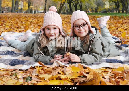 Deux sœurs jumelles heureuses s'allongent sur une couverture à carreaux dans un parc d'automne. Filles souriant et regardant la caméra. Photo horizontale Banque D'Images