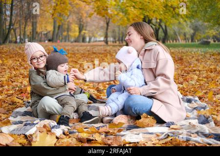 La grande famille. Maman avec ses trois enfants passent du temps assis sur une couverture dans le parc d'automne. Photo horizontale Banque D'Images