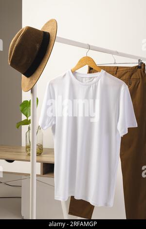 T-shirt blanc, chapeau et pantalon brun accroché à la tringle à vêtements avec espace de copie sur fond blanc Banque D'Images