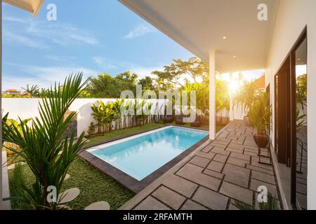 Vue sur villa tropicale avec jardin, piscine et salon ouvert au lever du soleil. Banque D'Images