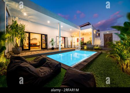 Vue sur la villa tropicale avec jardin, piscine et salon ouvert au coucher du soleil. Banque D'Images