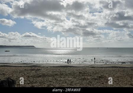 Oxwich Bay Beach par une journée ensoleillée et nuageuse en août avec des gens promenant leurs chiens et la lumière du soleil éclaboussant sur la mer. Trois bateaux au loin Banque D'Images