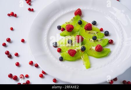 nourriture de noël pour les enfants. plat blanc avec sapin de noël fait de kiwi, framboises, cowberry et huckleberry. Photo de haute qualité Banque D'Images