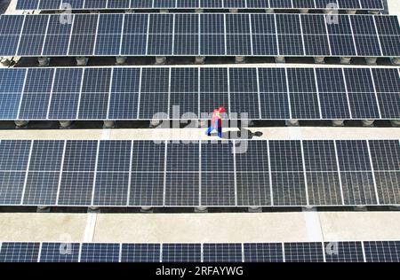 HANGZHOU, CHINE - 2 AOÛT 2023 - des employés d'une société d'alimentation électrique vérifient les installations de production d'énergie photovoltaïque sur le toit d'une école primaire Banque D'Images