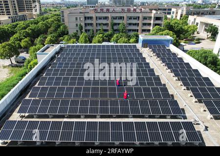 HANGZHOU, CHINE - 2 AOÛT 2023 - des employés d'une société d'alimentation électrique vérifient les installations de production d'énergie photovoltaïque sur le toit d'une école primaire Banque D'Images