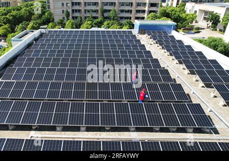 HANGZHOU, CHINE - 2 AOÛT 2023 - des employés d'une société d'alimentation électrique vérifient les installations de production d'énergie photovoltaïque sur le toit d'une école primaire Banque D'Images
