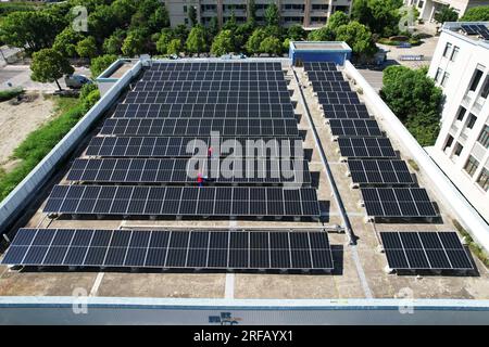HANGZHOU, CHINE - 2 AOÛT 2023 - des employés d'une société d'alimentation électrique vérifient les installations de production d'énergie photovoltaïque sur le toit d'une école primaire Banque D'Images