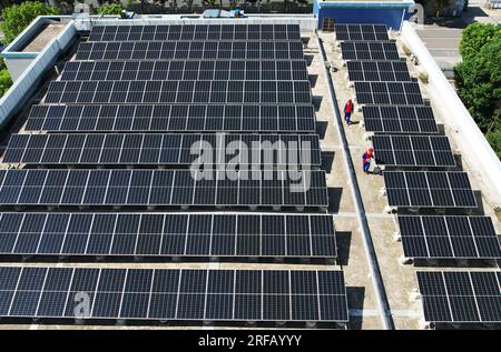 HANGZHOU, CHINE - 2 AOÛT 2023 - des employés d'une société d'alimentation électrique vérifient les installations de production d'énergie photovoltaïque sur le toit d'une école primaire Banque D'Images