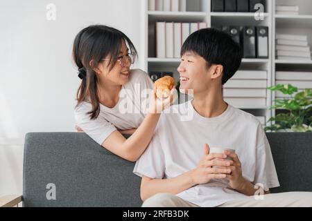 Les jeunes couples passent des vacances dans le salon. Le jeune homme portait des vêtements confortables, montrant son visage, satisfait du goût des collations Banque D'Images