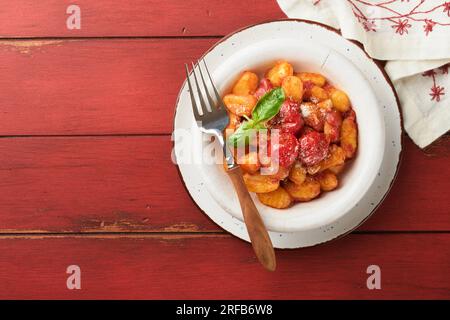 Gnocchi de pomme de terre. Gnocchi de pommes de terre maison traditionnels avec sauce tomate, basilic et fromage parmesan sur fond de table de cuisine rustique rouge. Traditionnel I Banque D'Images