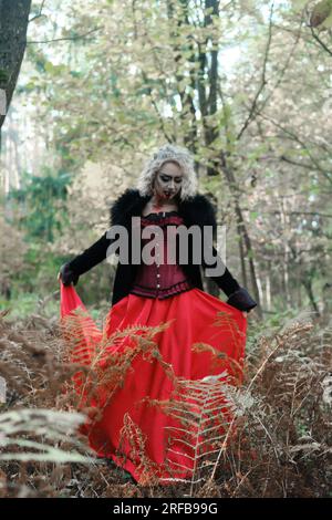 Une femme en forme de vampire ou de sorcière en robe médiévale marche dans la forêt. Concentrez-vous sur les plantes. Photo verticale Banque D'Images
