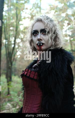 Une femme en forme de vampire ou de sorcière en robe médiévale marche dans la forêt. Vampire à la recherche d'une victime. Photo verticale Banque D'Images