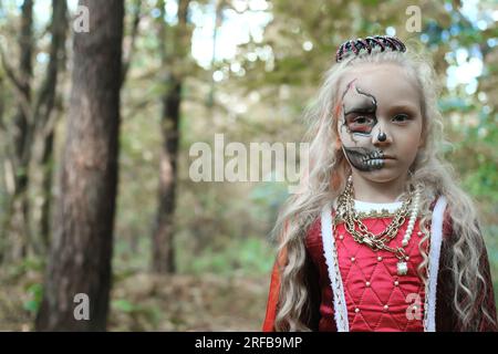 Une fillette pose dans une forêt dans une robe médiévale à l'image d'une princesse morte maquillée sur son visage. fille regardant la caméra. Pho. Horizontale Banque D'Images