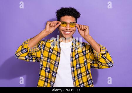 Photo de charmant mec attrayant habillé à carreaux jaune chemise bras lunettes sombres isolé fond de couleur violet Banque D'Images