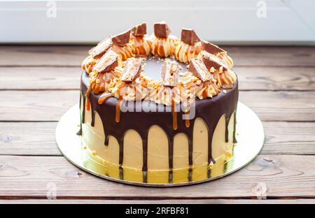 Gâteau à la crème au beurre de cacahuète avec chocolat fondu, barres de bonbons, bouchées de cacahuètes et caramel salé sur fond de bois Banque D'Images