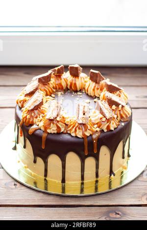 Gâteau à la crème au beurre de cacahuète avec chocolat fondu, barres de bonbons, bouchées de cacahuètes et caramel salé sur fond de bois Banque D'Images