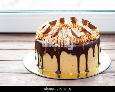 Gâteau à la crème au beurre de cacahuète avec chocolat fondu, barres de bonbons, bouchées de cacahuètes et caramel salé sur fond de bois Banque D'Images