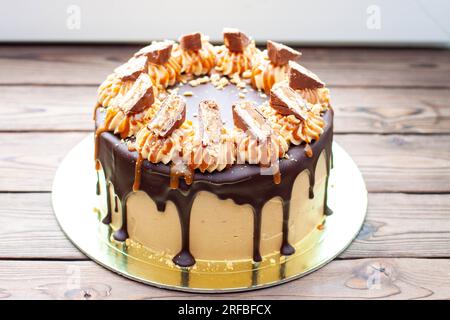 Gâteau à la crème au beurre de cacahuète avec chocolat fondu, barres de bonbons, bouchées de cacahuètes et caramel salé sur fond de bois Banque D'Images