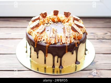 Gâteau à la crème au beurre de cacahuète avec chocolat fondu, barres de bonbons, bouchées de cacahuètes et caramel salé sur fond de bois Banque D'Images