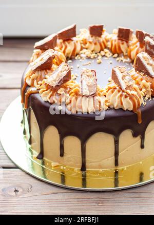 Gâteau à la crème au beurre de cacahuète avec chocolat fondu, barres de bonbons, bouchées de cacahuètes et caramel salé sur fond de bois Banque D'Images