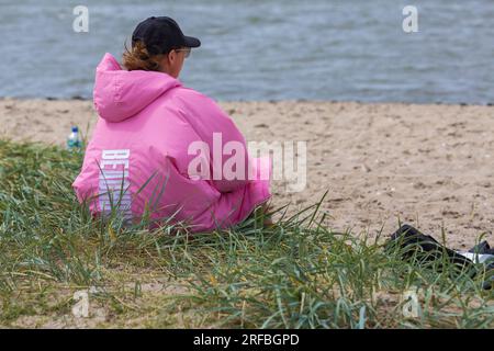 Femme portant une veste rose assise sur la plage à Sandbanks, Poole, Dorset UK en juillet Banque D'Images