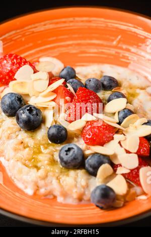 Flocons d'avoine avec des myrtilles, des amandes et des fraises dans une assiette orange. Gros plan. Vue d'en haut. Banque D'Images