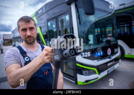 Rostock, Allemagne. 02 août 2023. Sebastian Schuh tient une prise de charge pour recharger un bus électrique au nouveau dépôt de Rostocker Straßenbahn AG (RSAG). Après six mois de travaux de conversion, le site des autobus réguliers a été adapté pour les systèmes de propulsion alternatifs. Les bus peuvent être alimentés avec de l’énergie électrique et du biométhane, et le plan est de convertir progressivement tous les services d’autobus en systèmes d’entraînement respectueux du climat au cours des prochaines années. Crédit : Jens Büttner/dpa/Alamy Live News Banque D'Images