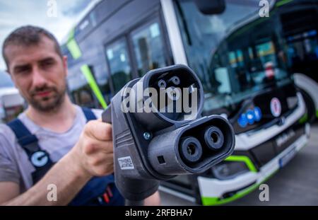 Rostock, Allemagne. 02 août 2023. Sebastian Schuh tient une prise de charge pour recharger un bus électrique au nouveau dépôt de Rostocker Straßenbahn AG (RSAG). Après six mois de travaux de conversion, le site des autobus réguliers a été adapté pour les systèmes de propulsion alternatifs. Les bus peuvent être alimentés avec de l’énergie électrique et du biométhane, et le plan est de convertir progressivement tous les services d’autobus en systèmes d’entraînement respectueux du climat au cours des prochaines années. Crédit : Jens Büttner/dpa/Alamy Live News Banque D'Images