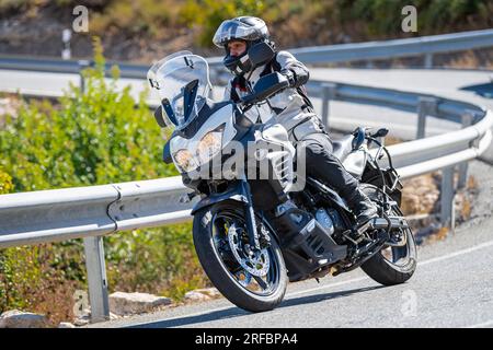 Pilote de moto prenant une courbe au premier plan, avec un fond de nature et de ciel bleu Banque D'Images