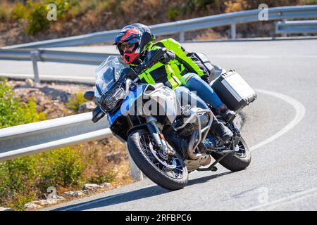Pilote de moto prenant une courbe au premier plan, avec un fond de nature et de ciel bleu Banque D'Images